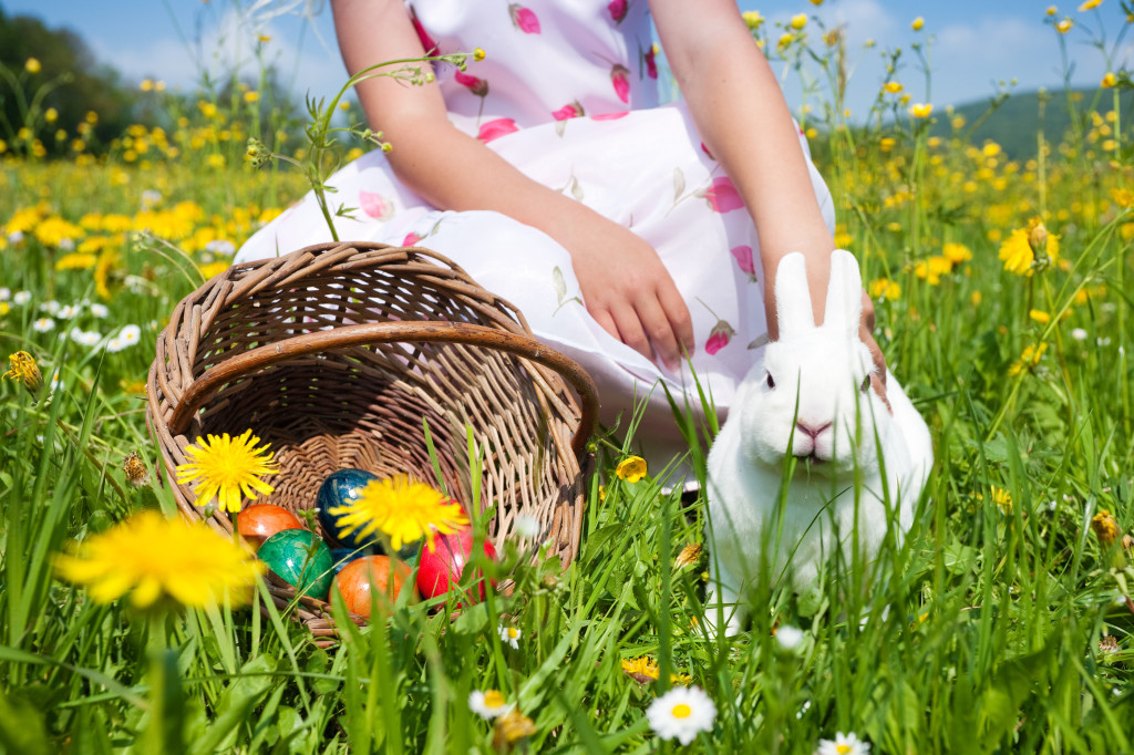 Child petting the Easter bunny on a spring meadow, eggs in a bas