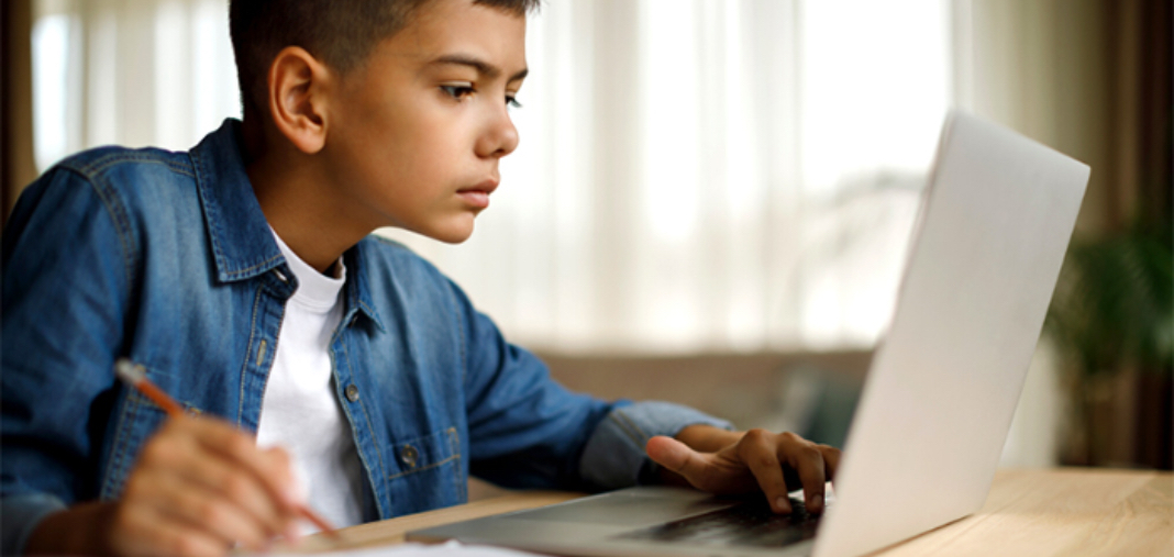 Niño latino haciendo apuntes y usando una laptop