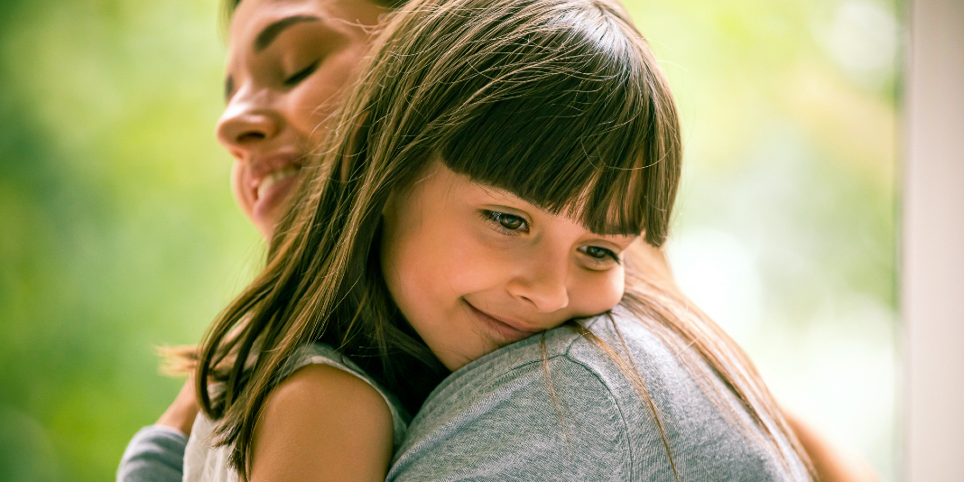 Mujer abrazando a su hija que está sonriendo