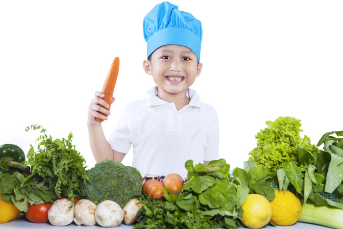 Niño con una zanahoria y rodeado de vegetales