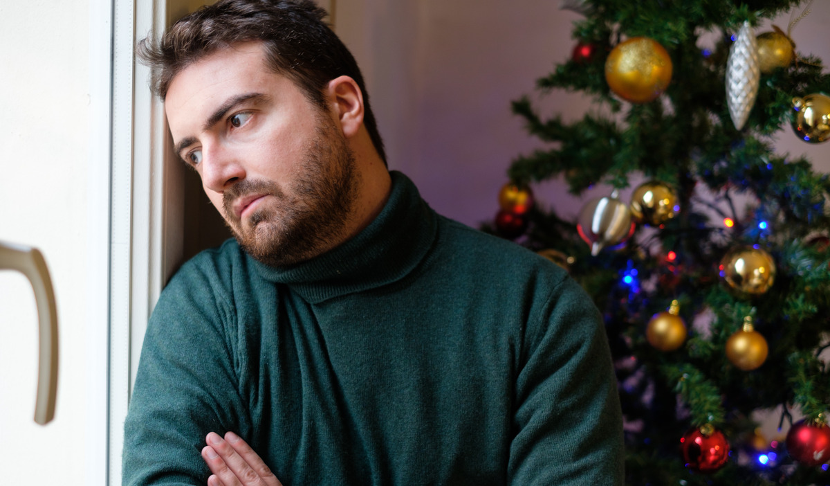 Hombre con mirada triste junto a un árbol de Navidad